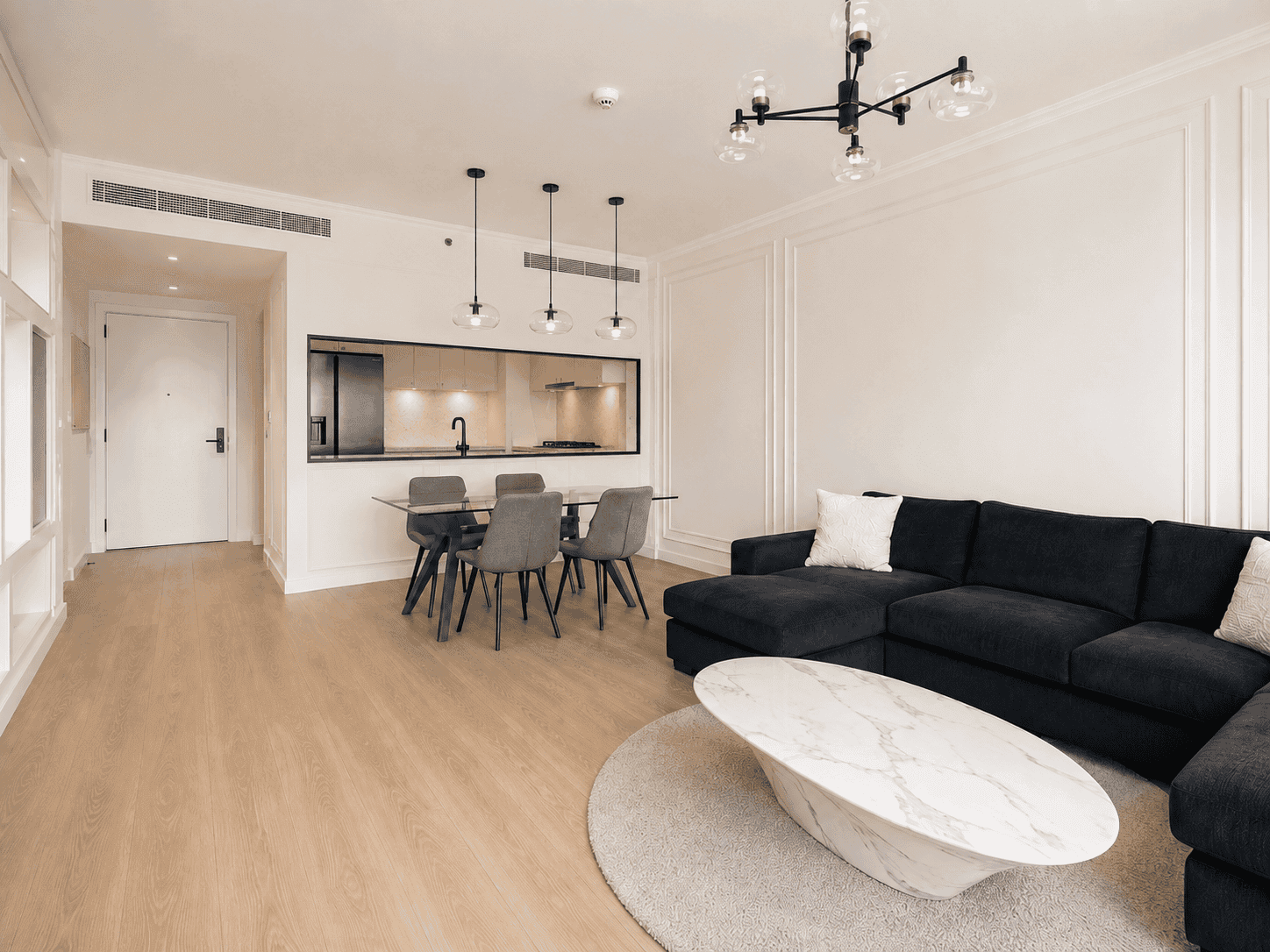 Renovated dining area with grey upholstered chairs and kitchen serving window in Acacia B apartment, Dubai Hills Estate