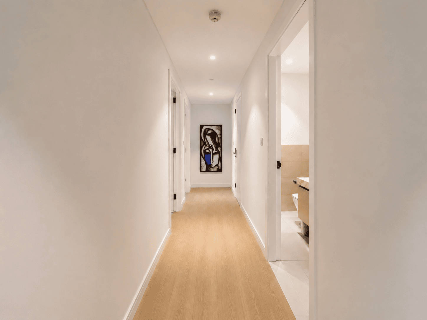 Bright renovated hallway with oak flooring, white walls and framed artwork in Park Heights apartment