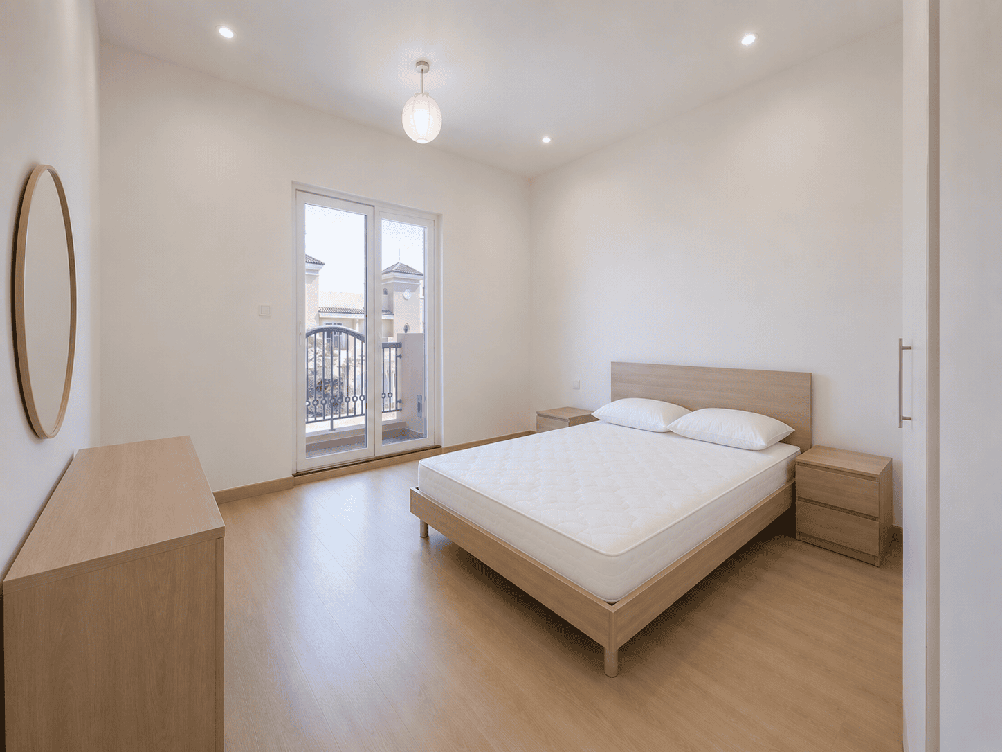 Bedroom with balcony door, oak dresser and round mirror in renovated Victory Heights villa, Dubai