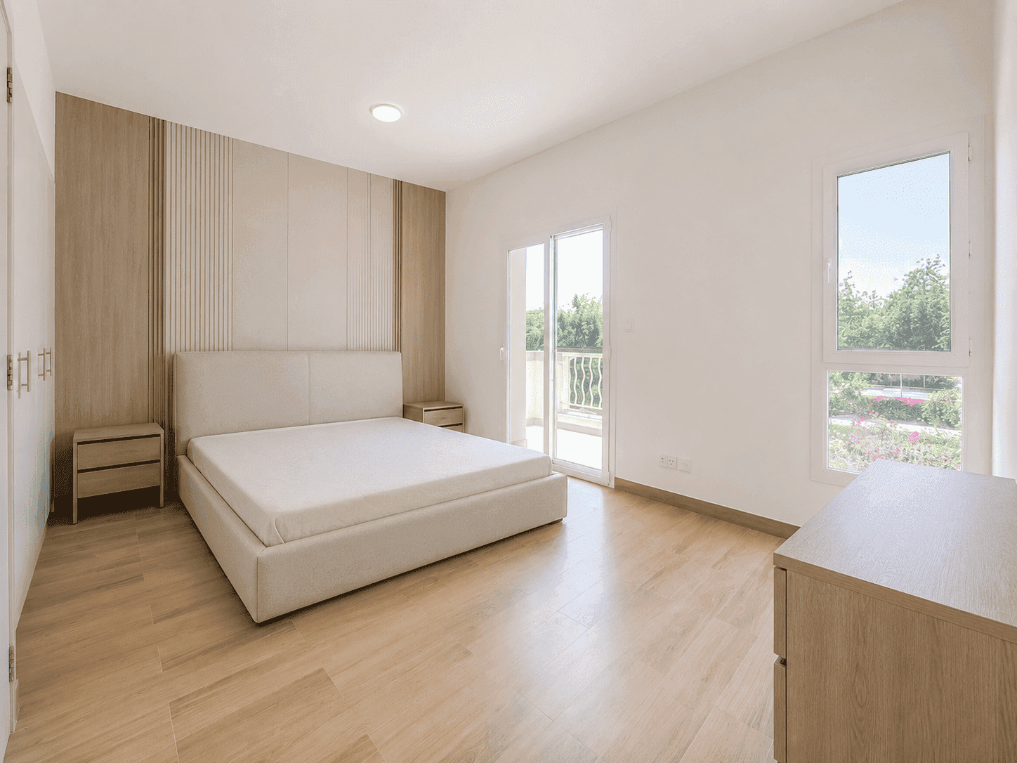 Master bedroom renovation with slatted oak feature wall, upholstered bed and balcony access in The Lakes villa