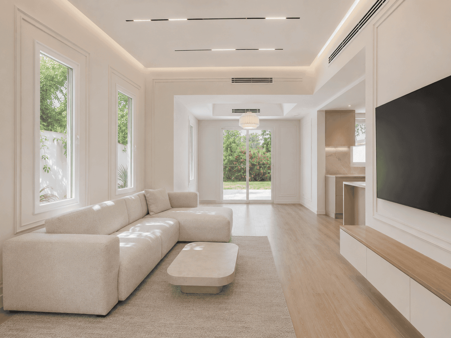 Renovated living hall with beige sectional sofa, magnetic track lighting and garden views in The Lakes villa