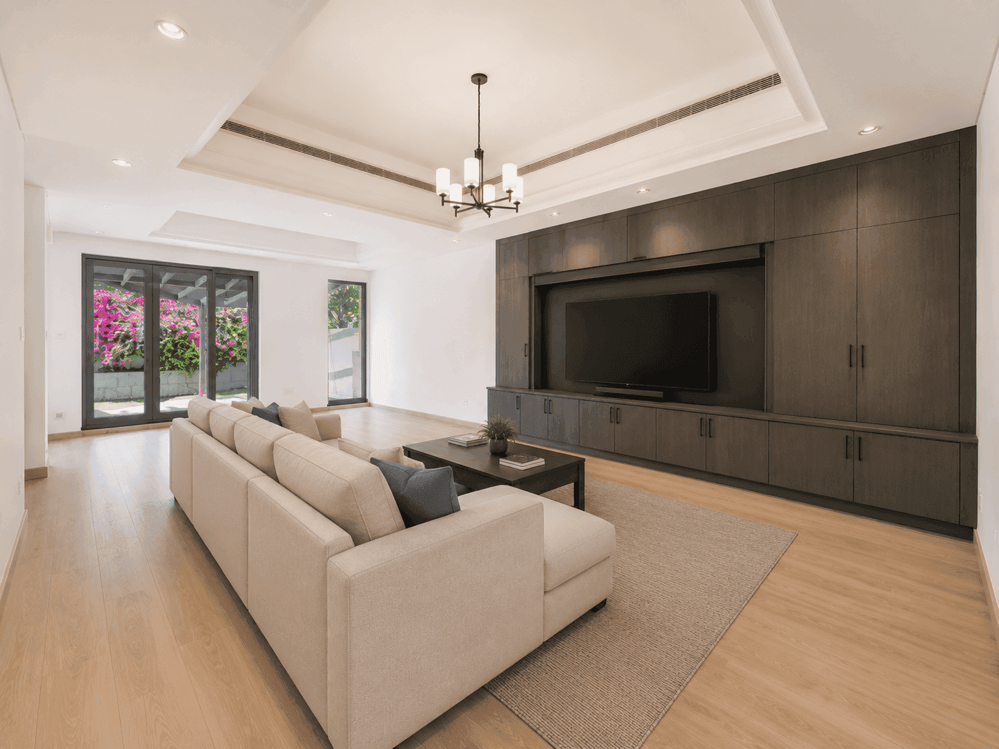 Family hall renovation with full-wall dark oak media unit, chandelier and garden doors in Victory Heights villa