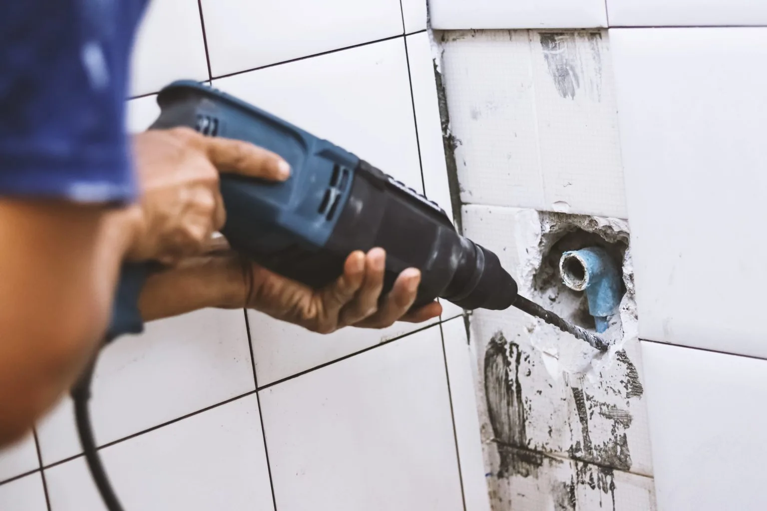 Bathroom strip out in Dubai with a technician drilling the tiled wall to expose the existing plumbing