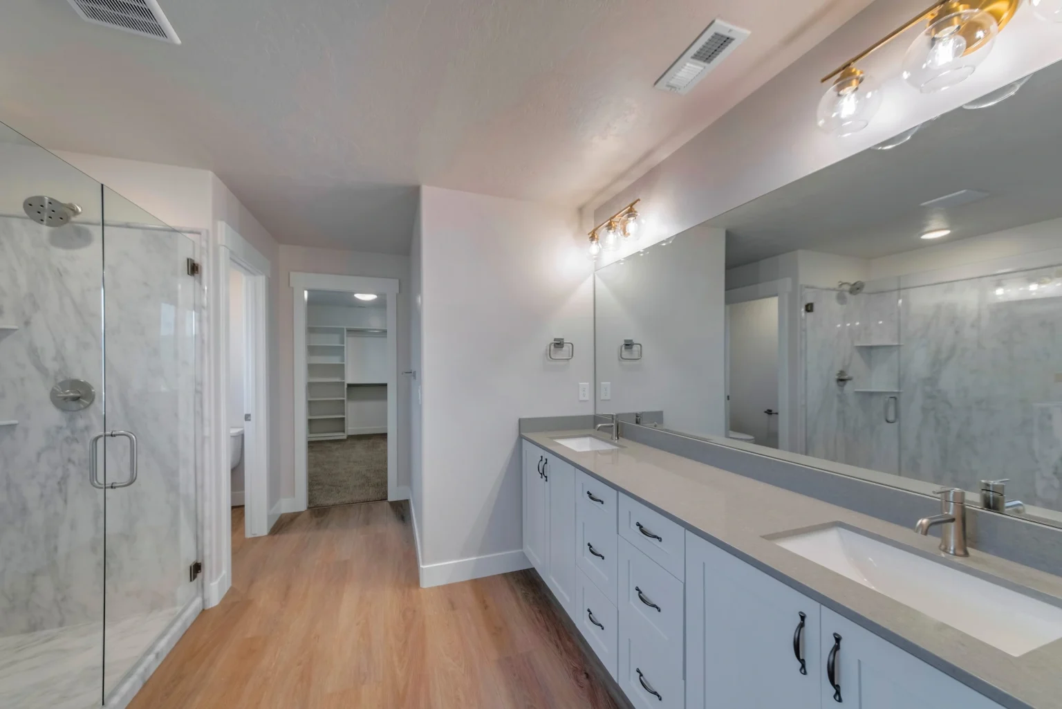 White shaker double vanity with grey quartz and a full height marble shower in a full bathroom remodel in Dubai