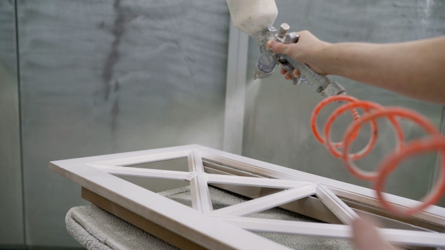 Spray gun applying a white finish to a framed timber panel