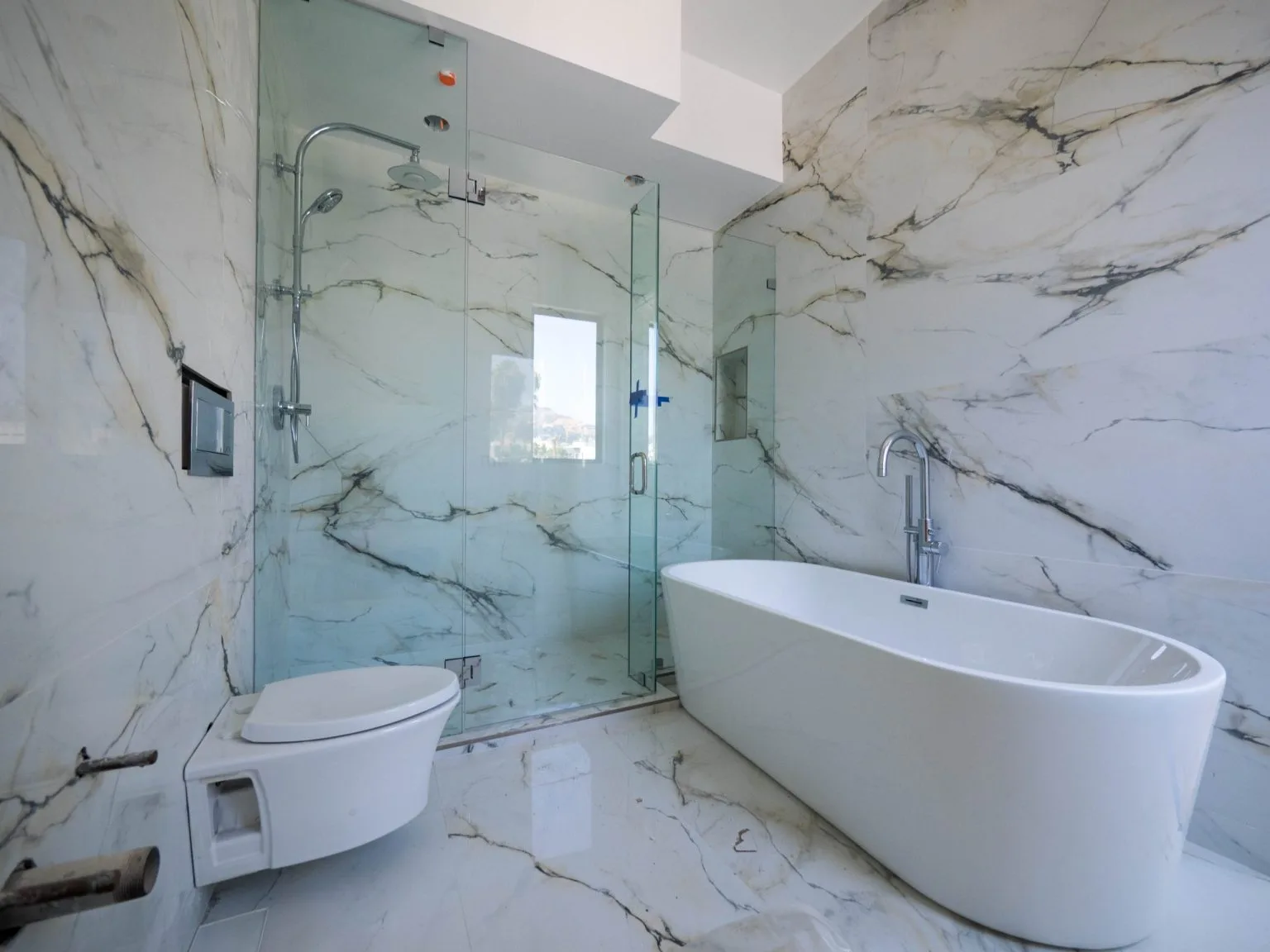 Frameless glass shower screen beside a freestanding bath in a marble Dubai bathroom