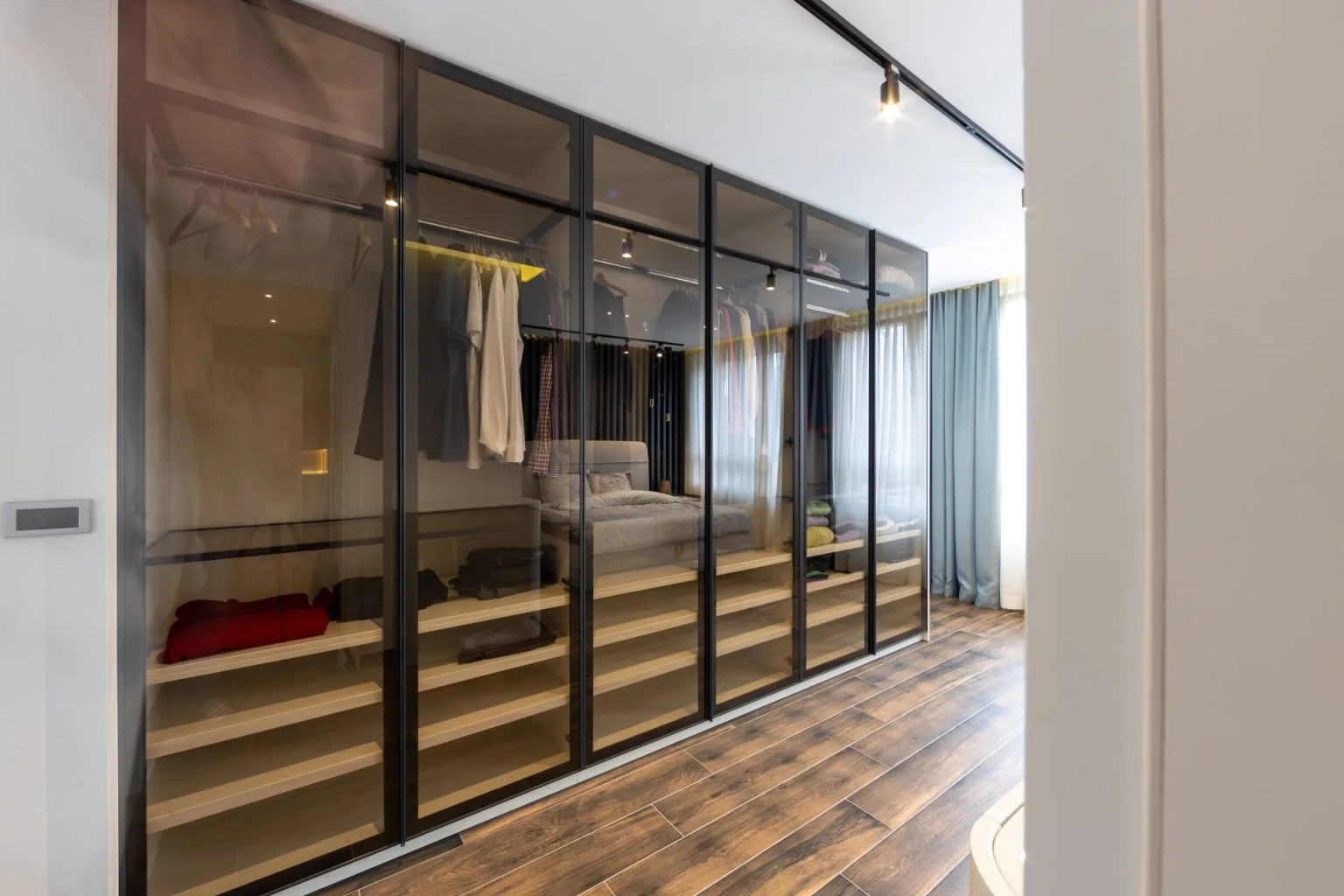 Walk in wardrobe with smoked glass black framed display doors built by a custom joinery company in Dubai