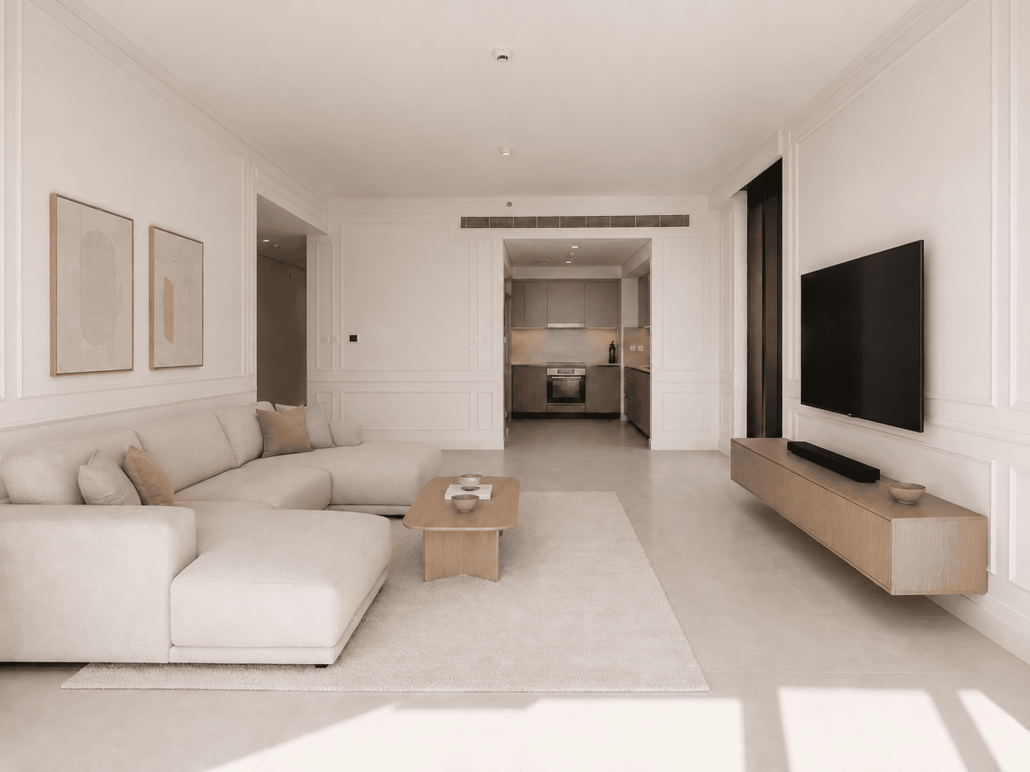 Creek Harbour renovation showing a completed apartment living room with wall panelling moulding, beige L-shaped sofa, floating wood TV console and open kitchen by Fitout Renovation Dubai