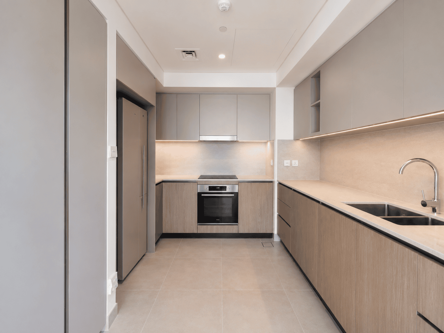 Kitchen renovation with greige and oak cabinetry, under-cabinet lighting and stone-look splashback in Dubai Creek Harbour
