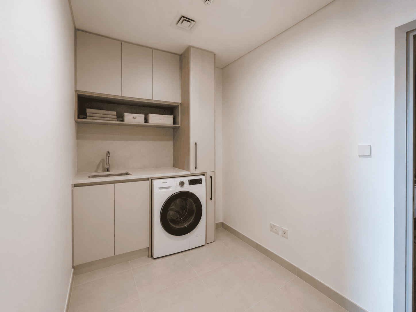 Renovated laundry room with built-in cabinets, sink, open shelf and washing machine housing in Dubai Creek Harbour