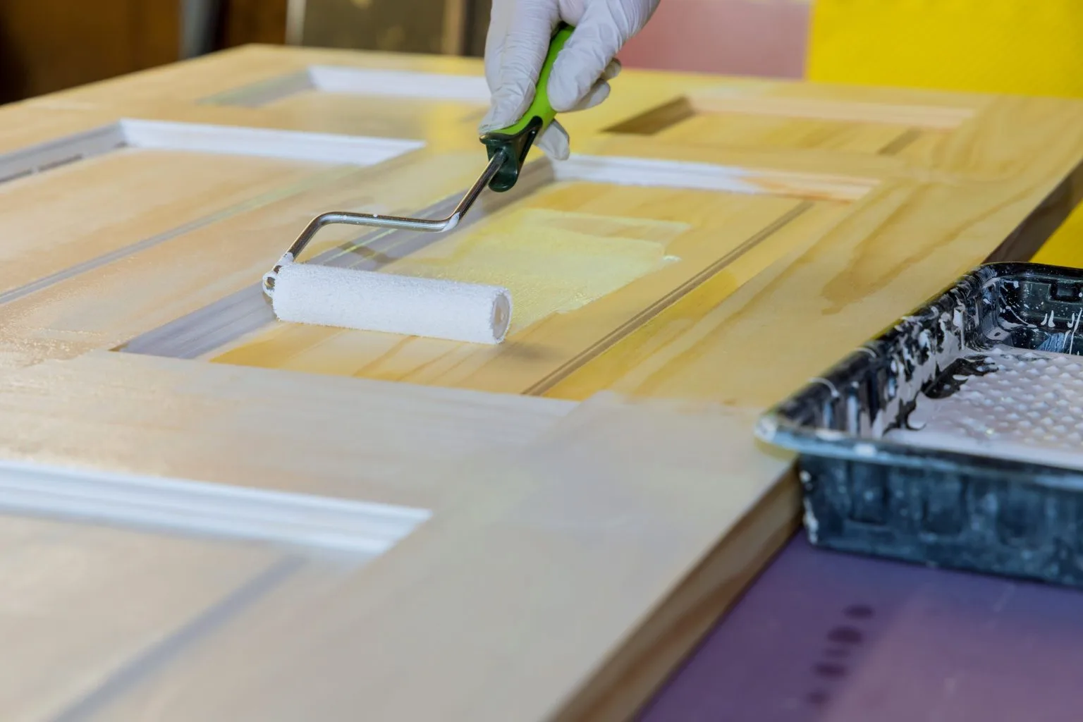 Roller applying fresh paint to a panelled door leaf