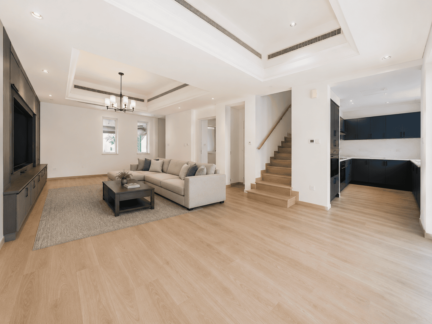 Victory Heights renovation showing a completed villa living room with gypsum tray ceiling, wood flooring, staircase and open-plan dark navy kitchen by Fitout Renovation Dubai