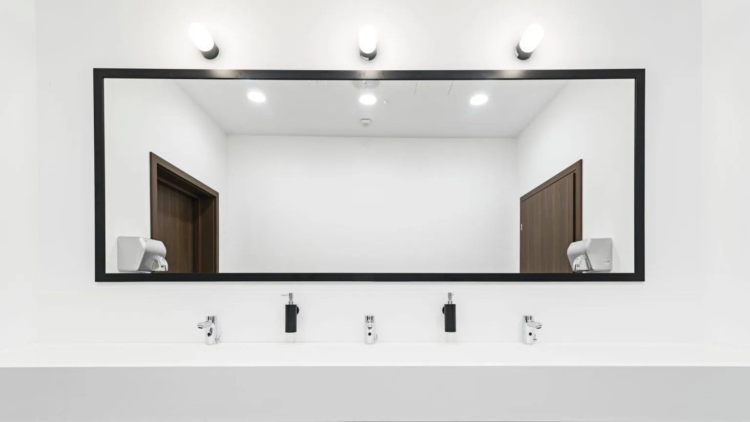 Long black-framed washroom mirror fitted above a trough basin in Dubai