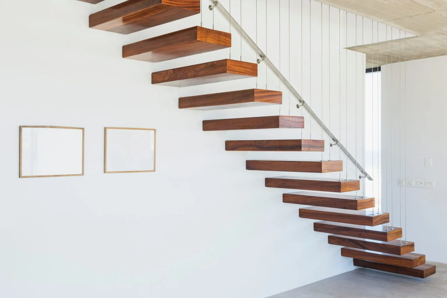 Floating walnut treads cantilevered from a white wall with a slim cable handrail