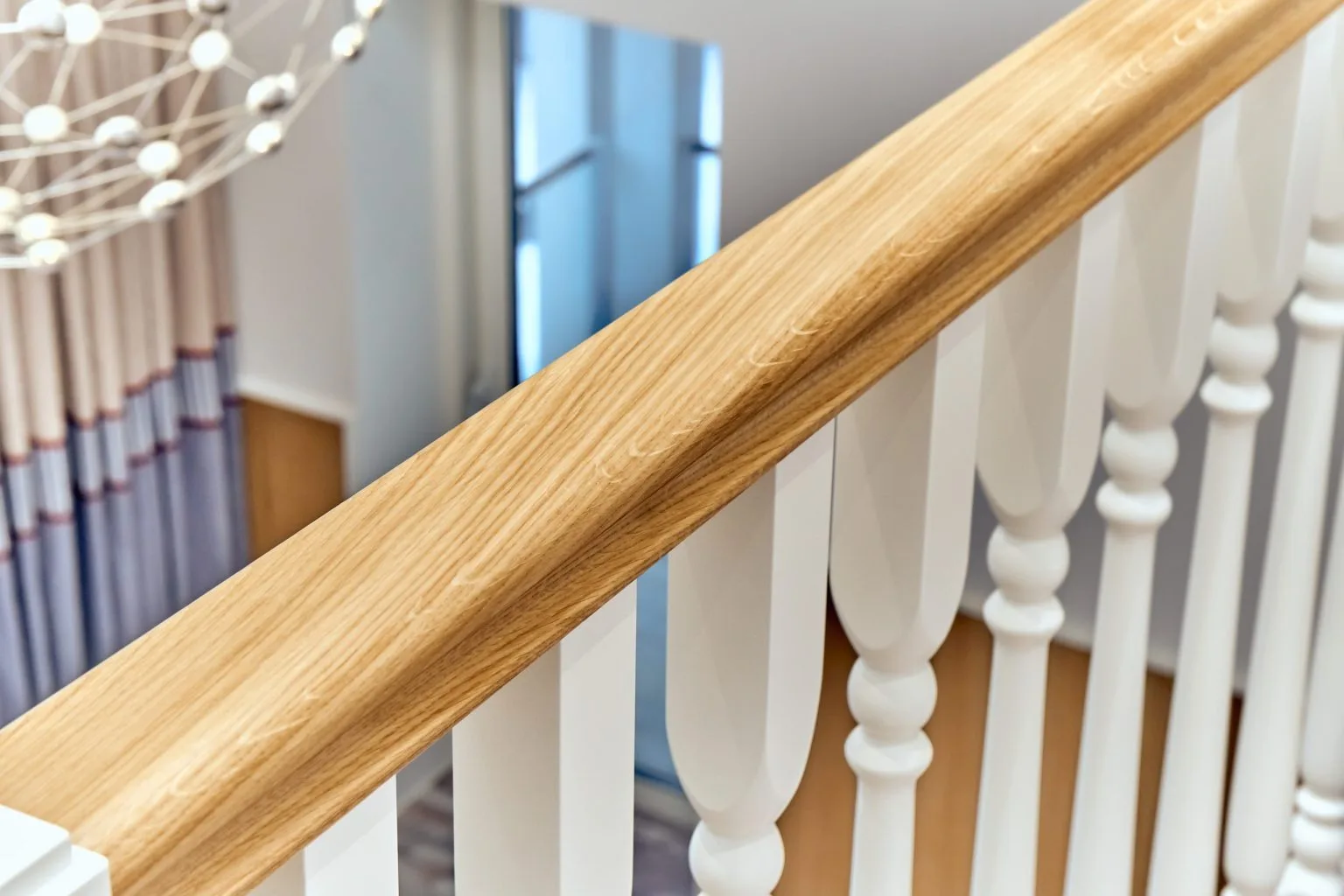 Close-up of a shaped oak handrail running past white turned balusters