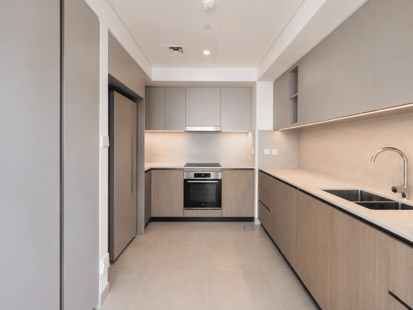 Kitchen renovation with greige and oak cabinetry, under-cabinet lighting and stone-look splashback in Dubai Creek Harbour