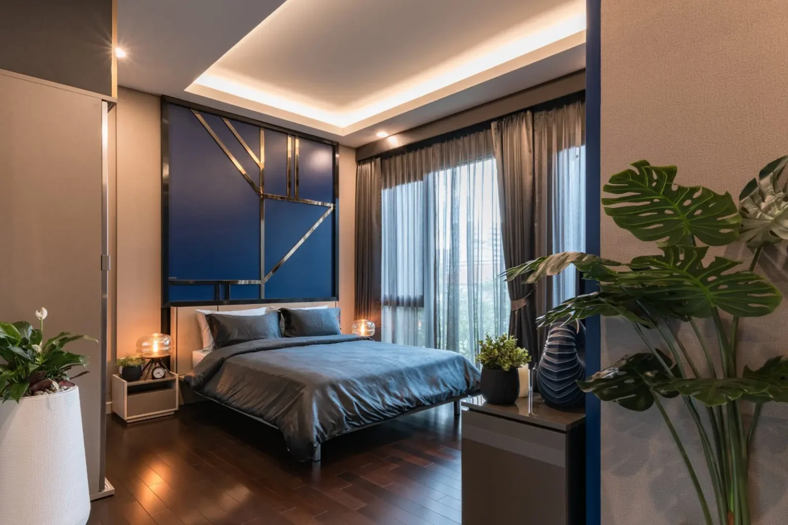 Modern bedroom with a deep blue painted feature wall, cove lighting and a hanging pendant