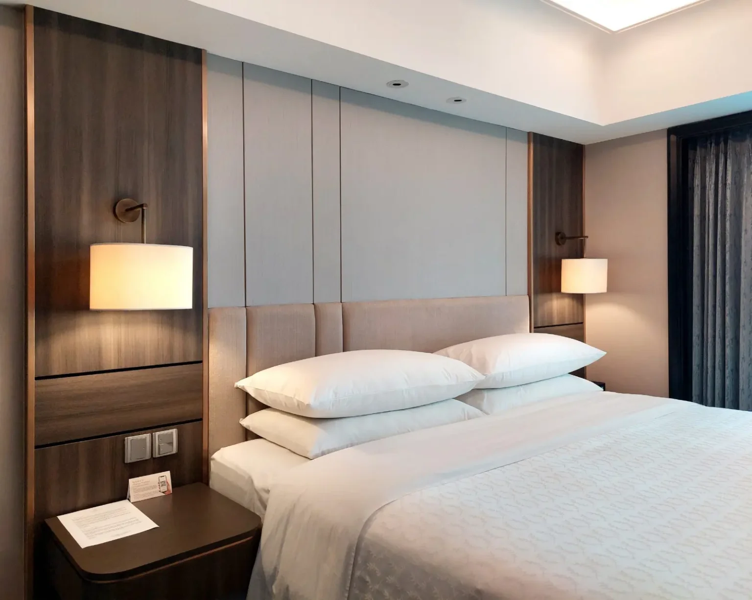 Padded headboard wall panelling with bronze reading sconces in a hotel-style bedroom