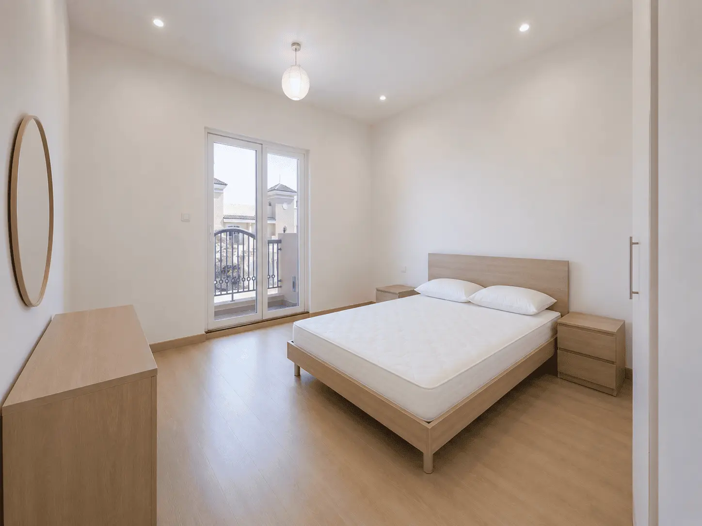 Bedroom with balcony door, oak dresser and round mirror in renovated Victory Heights villa, Dubai