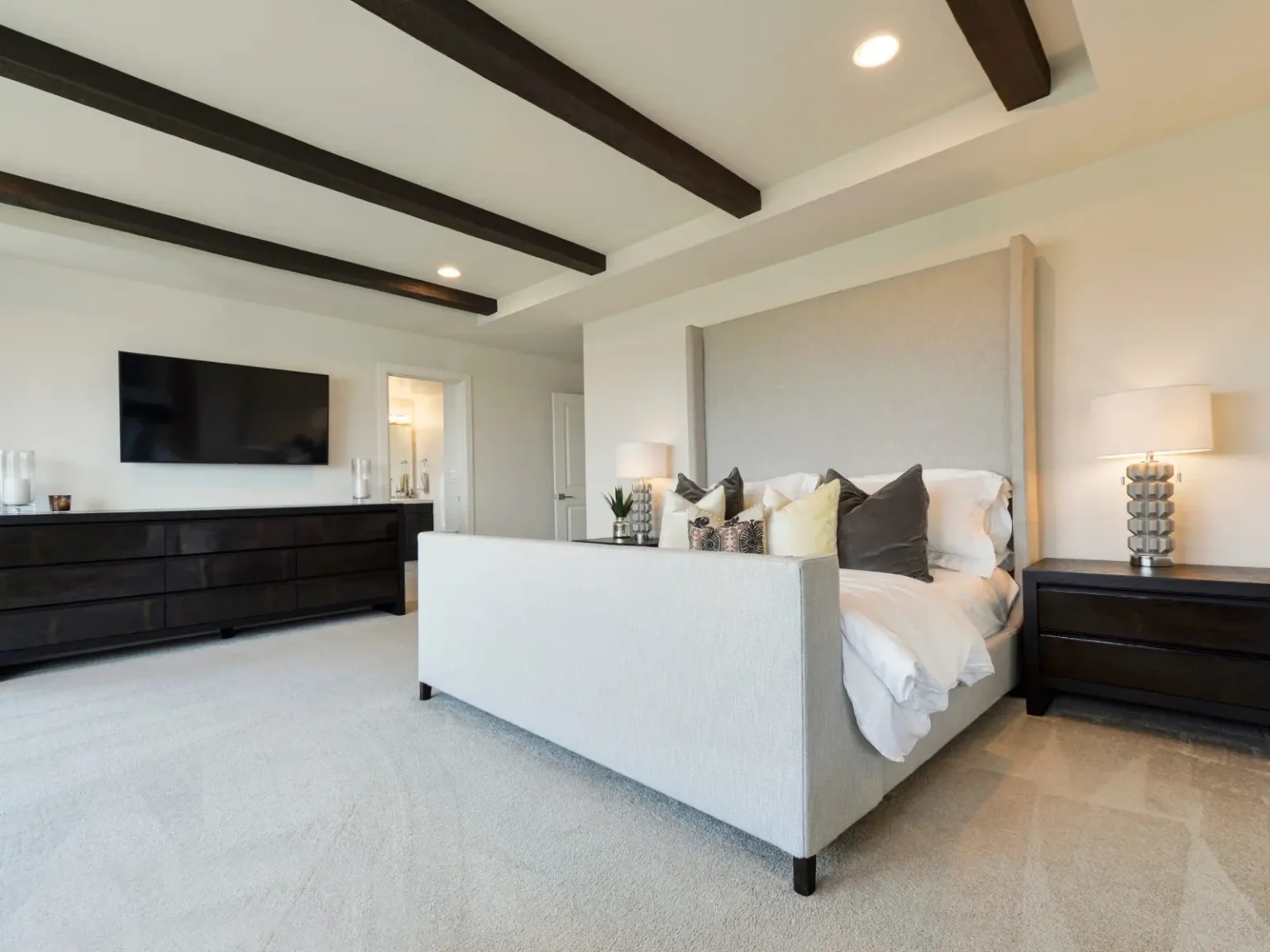 Villa master bedroom with exposed timber ceiling beams and a tall upholstered headboard