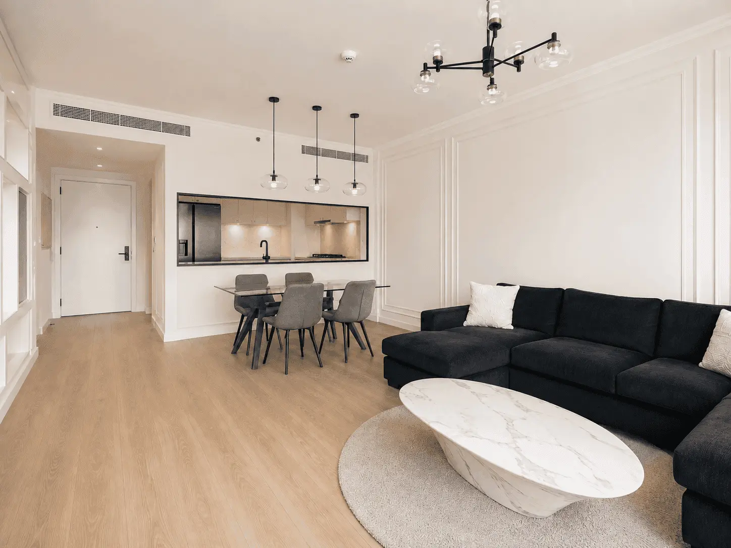 Renovated dining area with grey upholstered chairs and kitchen serving window in Acacia B apartment, Dubai Hills Estate