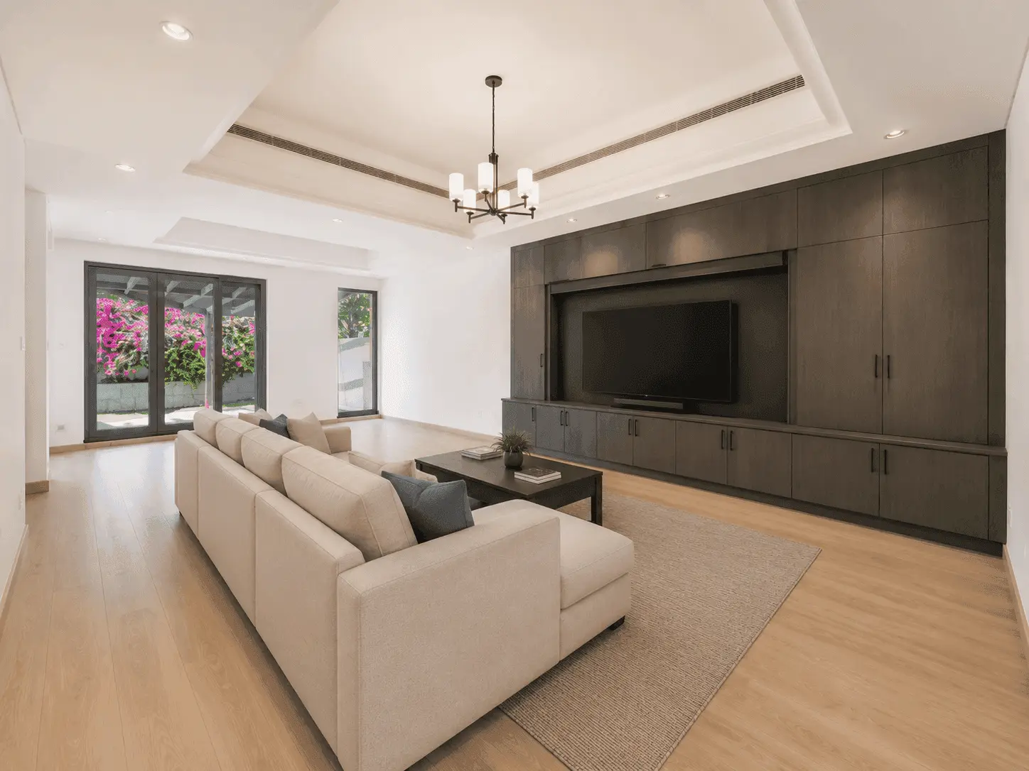 Family hall renovation with full-wall dark oak media unit, chandelier and garden doors in Victory Heights villa