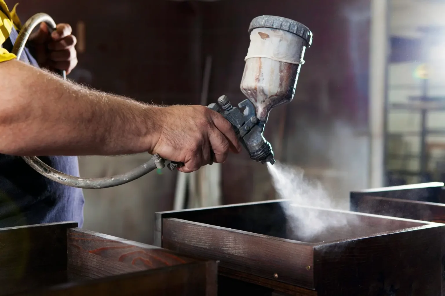 Craftsman spray-finishing a dark timber cabinet in Dubai for a furniture repaint