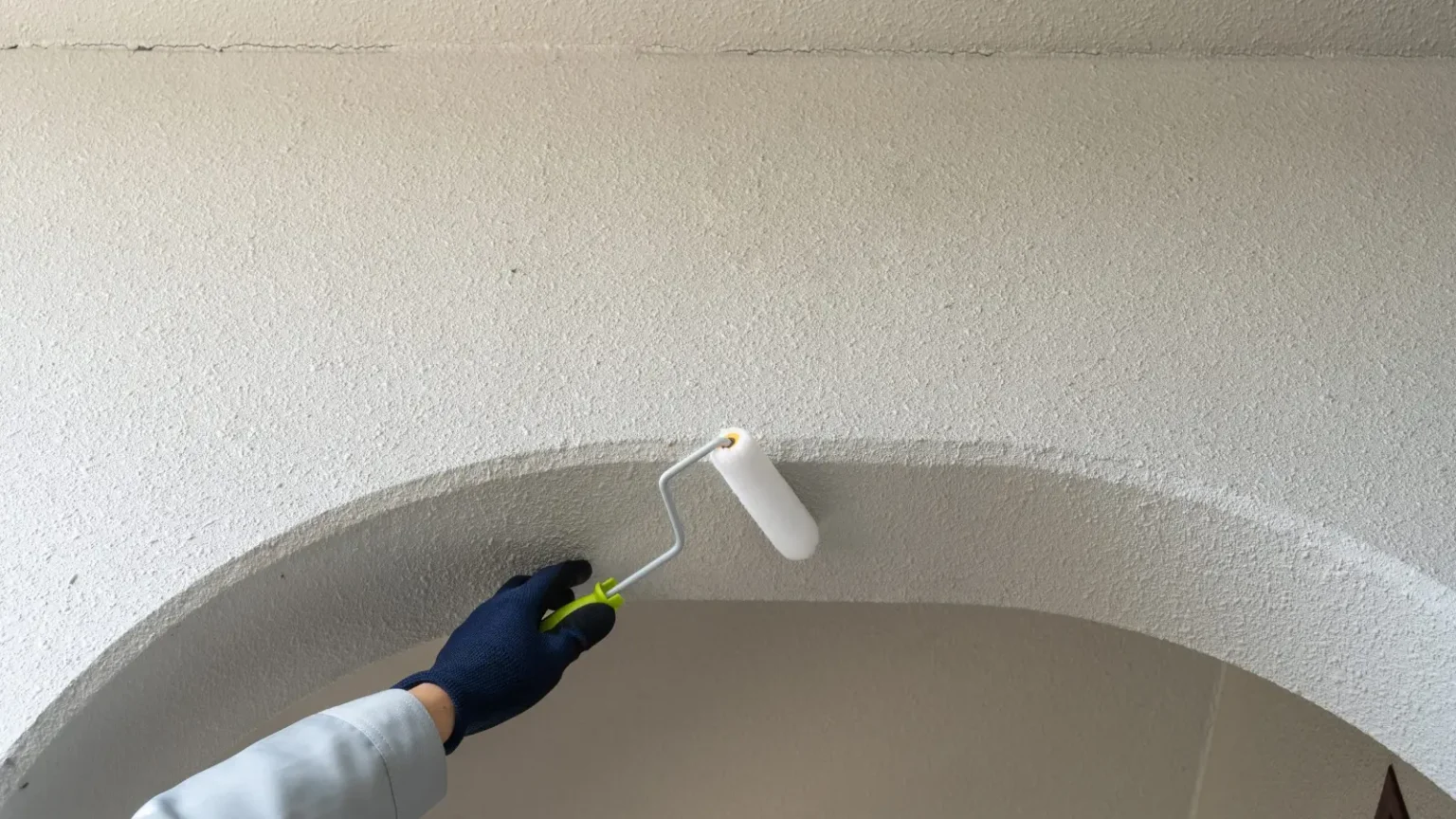 Roller applying white paint to a textured vaulted ceiling during ceiling painting works in Dubai
